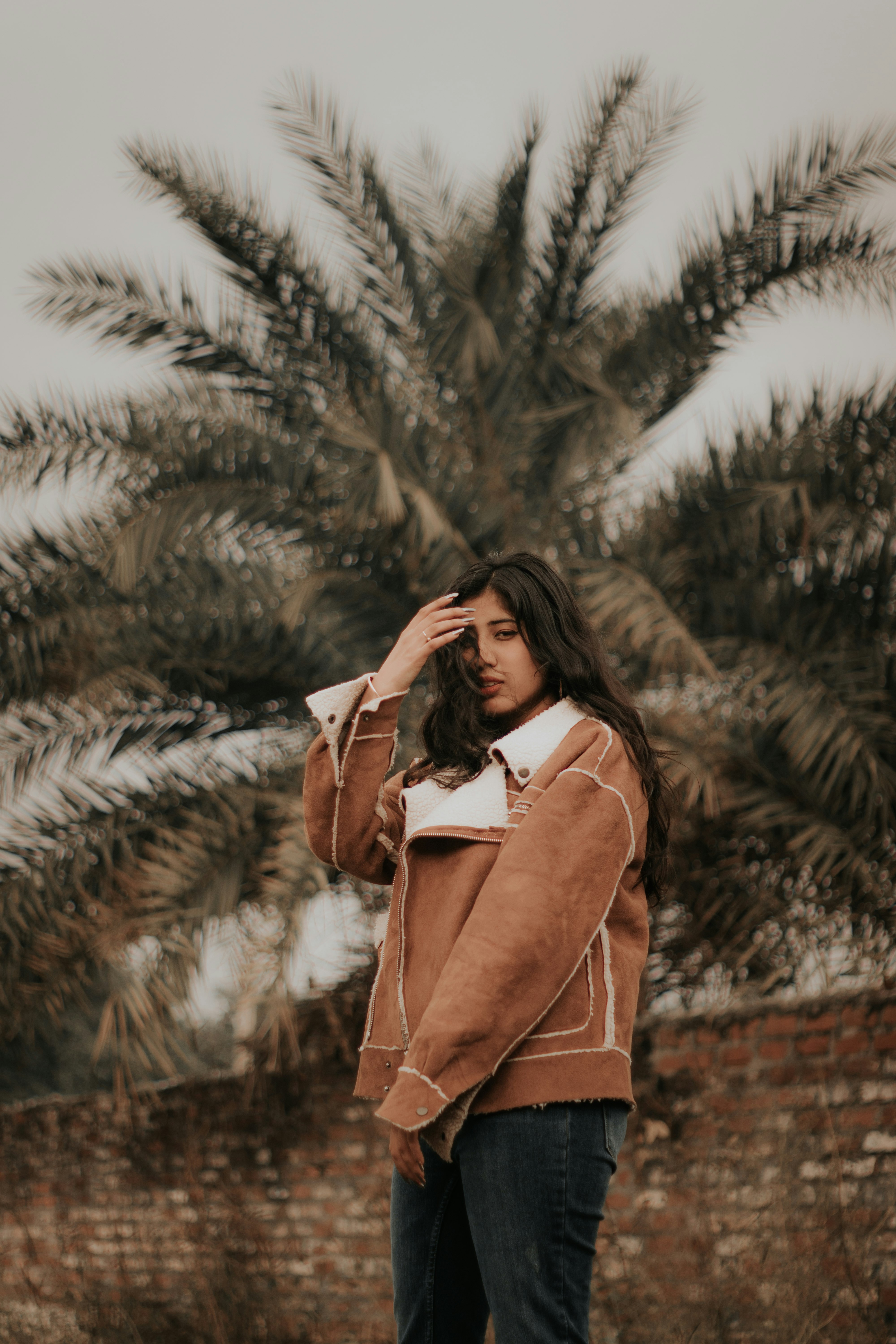 woman in brown coat standing near green pine tree during daytime